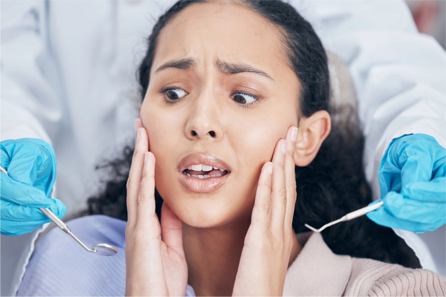 A woman looks distressed while a dentist prepares dental instruments nearby during a dental exam.