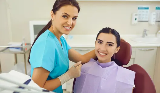 A dentist in scrubs smiling with a patient in a dental chair at SmileVibe Dentistry in Renton, WA.