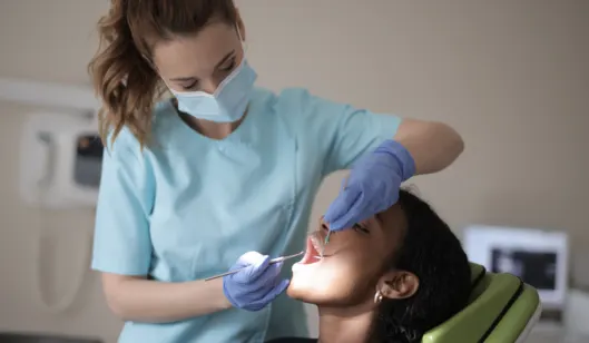 A dentist in scrubs and gloves is examining a patient's teeth in a dental office.