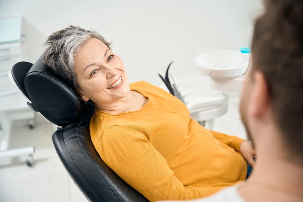 A smiling patient in a dental chair, wearing a yellow shirt, engages with a dentist in a bright treatment room.