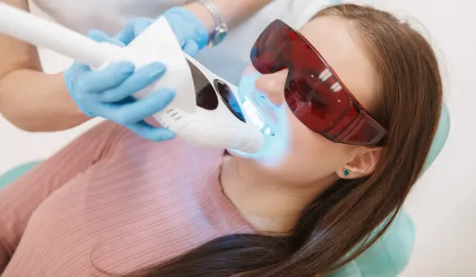 A patient wearing protective glasses receiving a dental treatment while lying in a dentist chair.