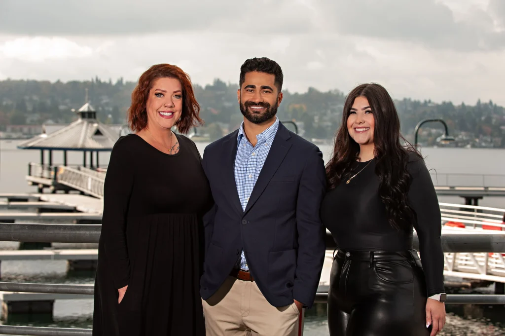 Three dental professionals stand together smiling on a dock with a waterfront view, promoting SmileVibe Dentistry in Renton.
