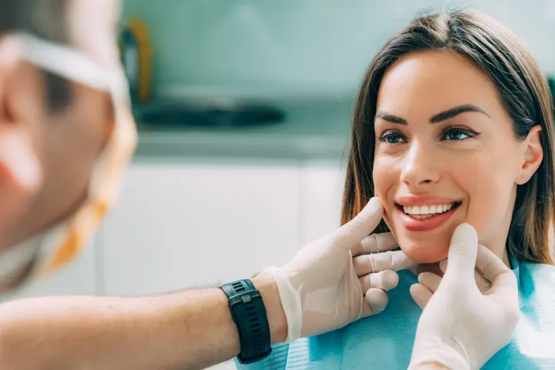 A dentist examining a smiling woman's teeth in a dental treatment room.