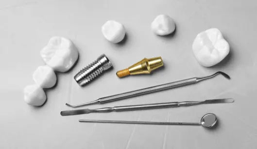 Dental tools, a dental implant screw, and artificial teeth displayed on a surface, related to SmileVibe Dentistry.