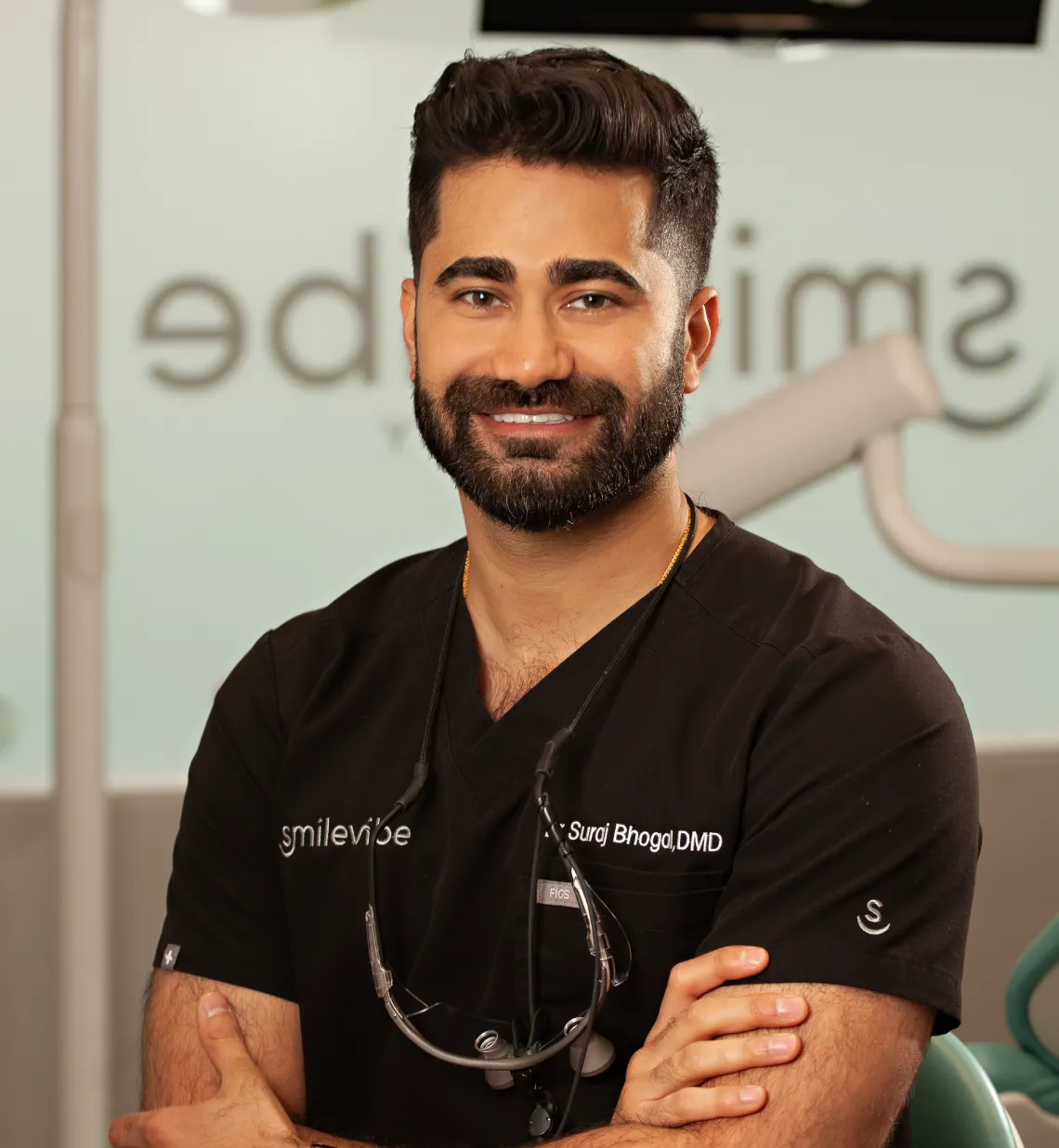A dentist in a black scrubs shirt smiles with arms crossed, standing in a dental office with "SmileVibe" signage in the background.