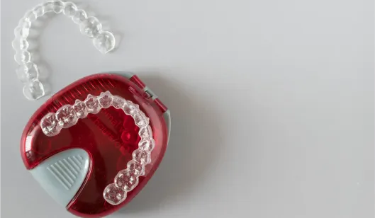 A clear aligner in a red case placed on a light surface, illustrating orthodontic treatment options.