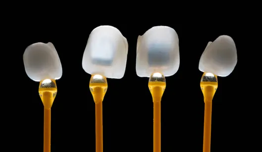 Four dental crowns on yellow applicators against a black background.