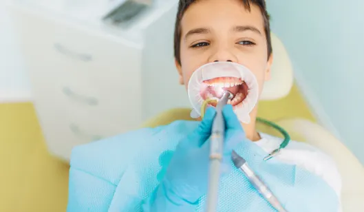 A young patient receiving dental treatment while lying in a dental chair, with a dental professional using equipment in their mouth.