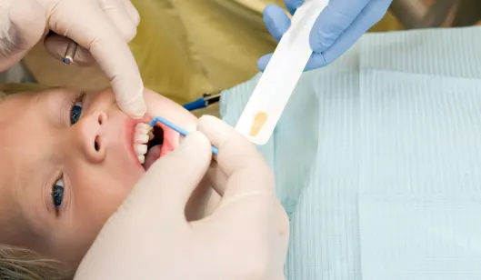 A dentist examining a child's teeth with a dental tool in a treatment room.