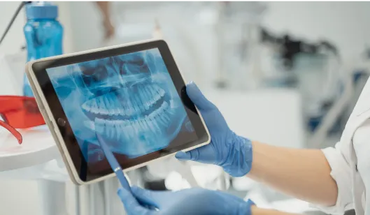 A dentist pointing to an X-ray of teeth displayed on a tablet in a dental office.